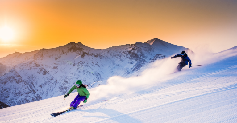 two people skiing down a mountain at sunset