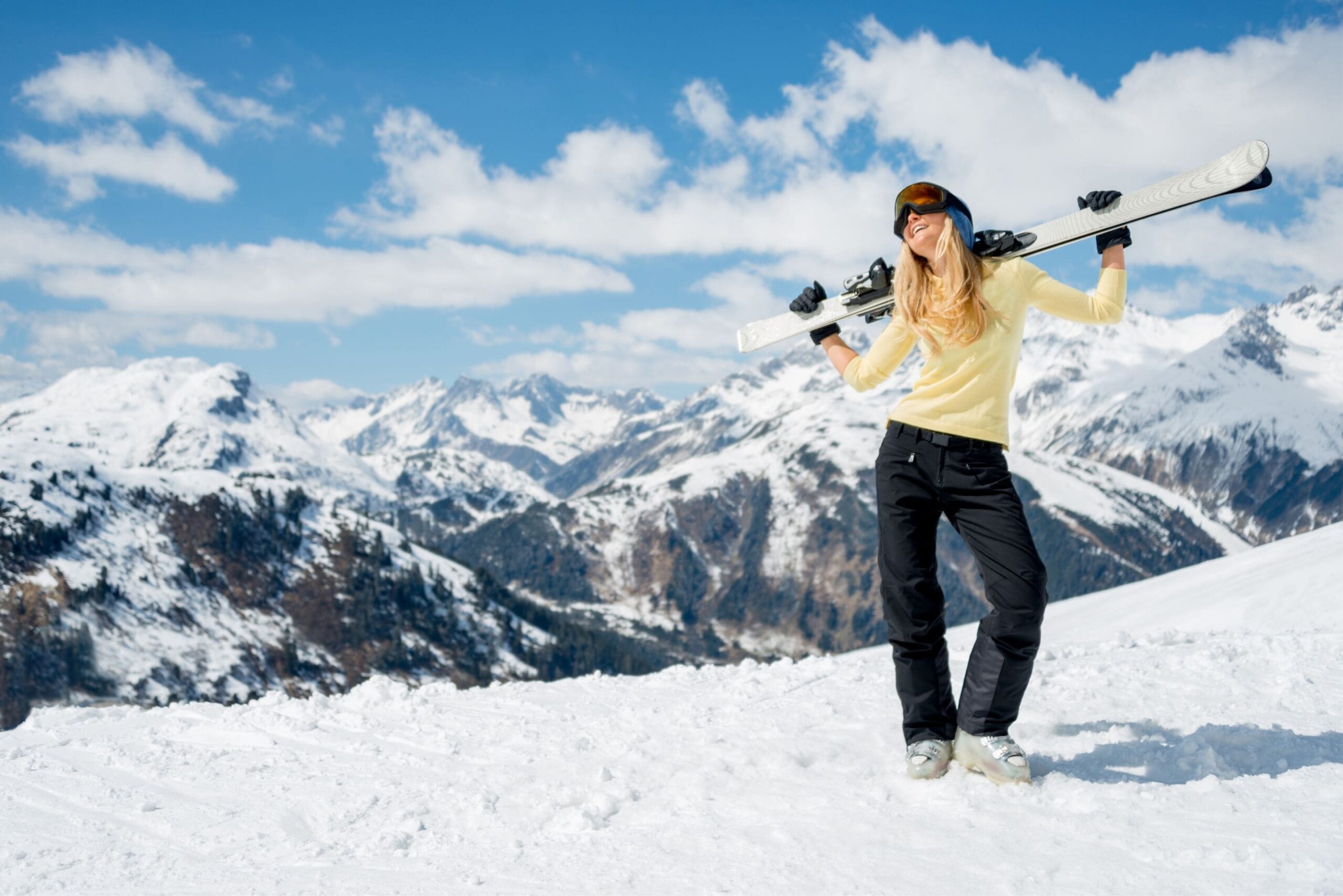 woman standing on a ski slope holding her skis behind her head