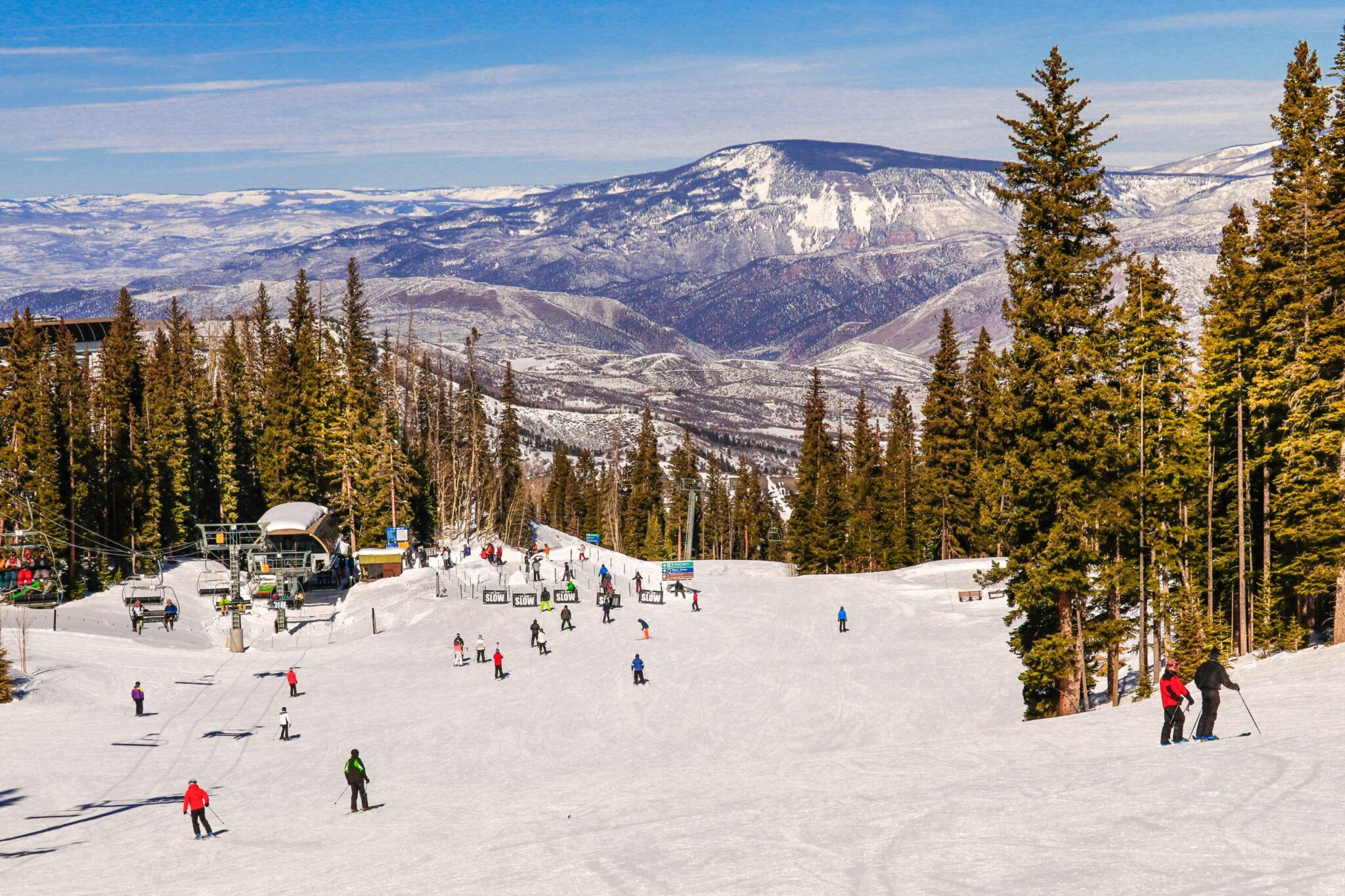 view from the top of a ski resort with people riding down the mountain and another mountain on the horizon