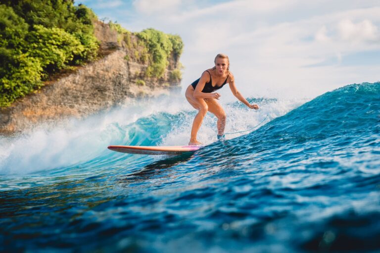 woman in a black bathing suit surfing with a cliff in the background