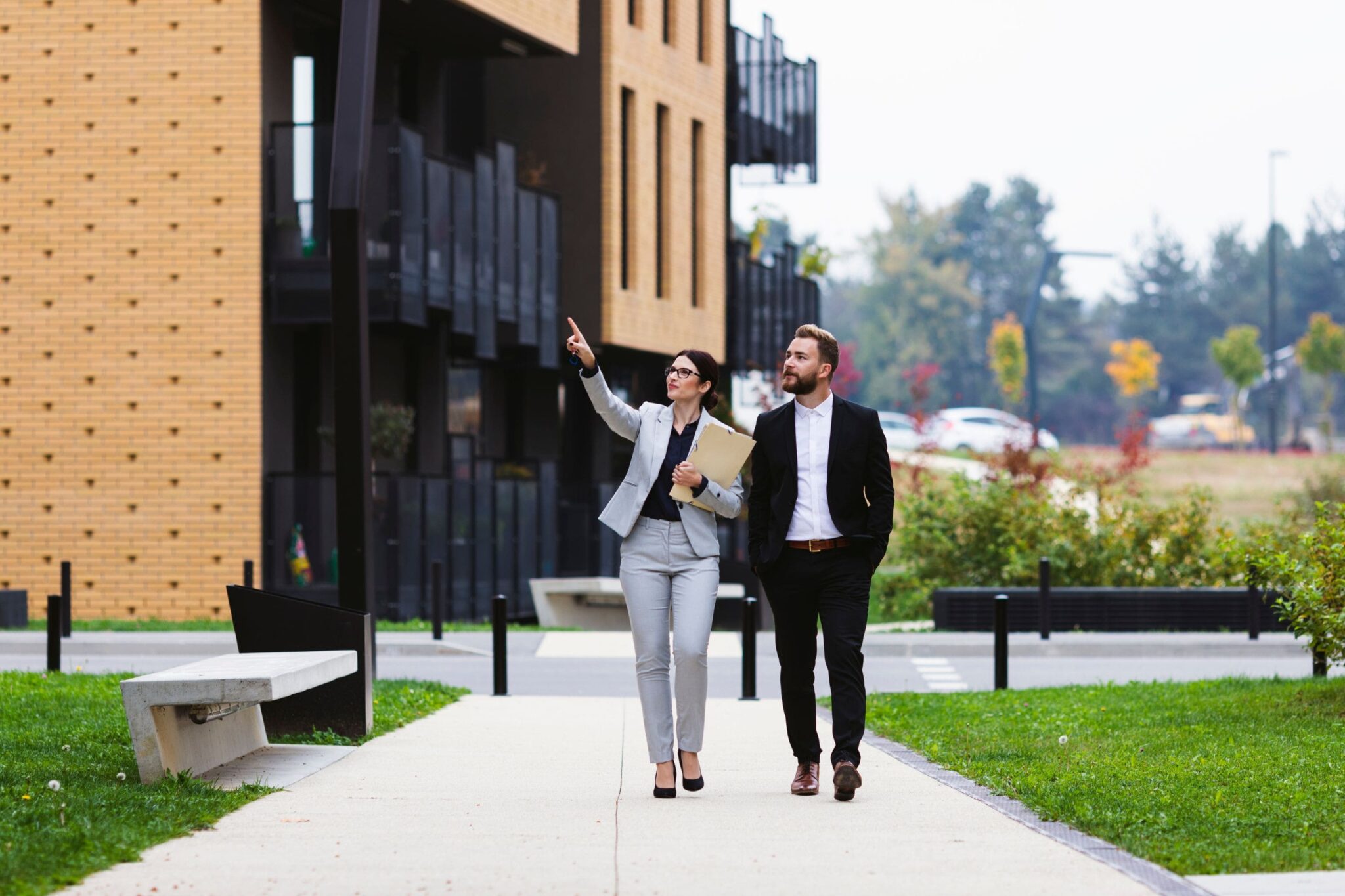 two people outside of a building walking the grounds and pointing things out