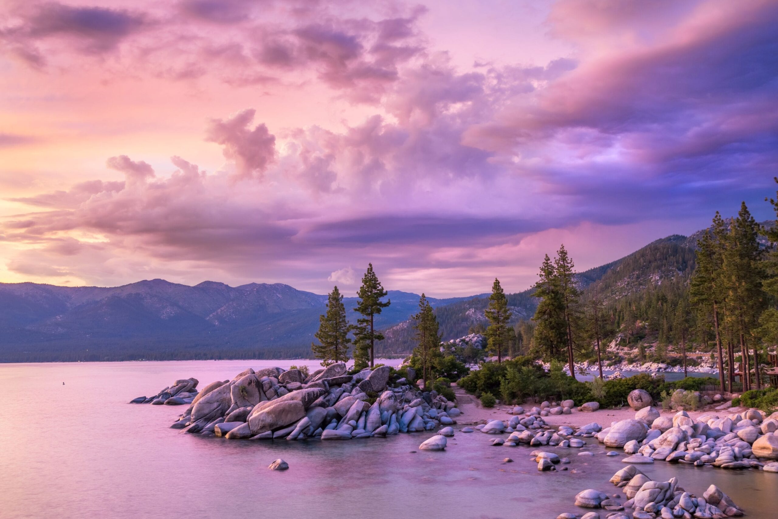 rocky outcropping coastline of Lake Tahoe against a orange and purple sunset sky