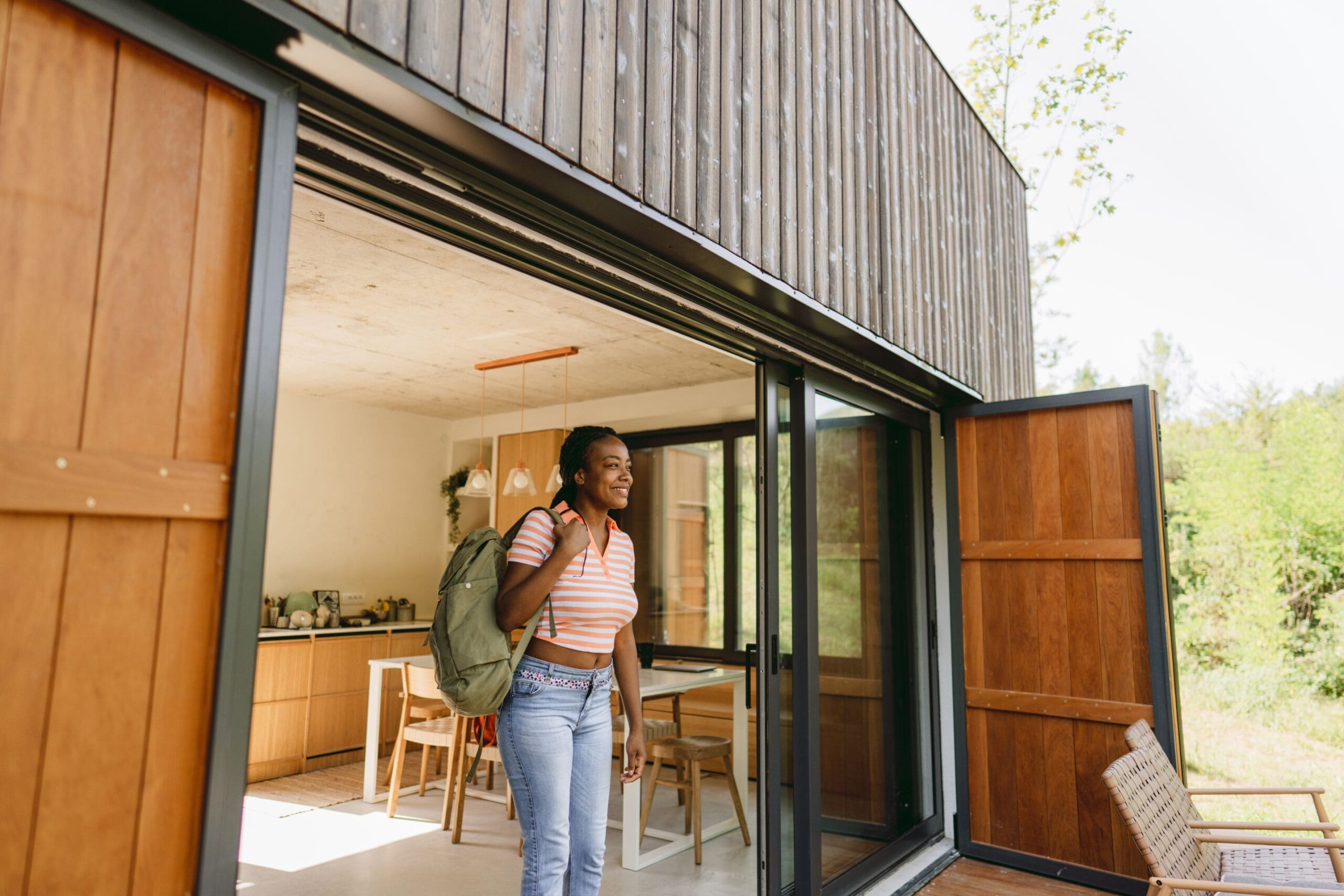 woman wearing a backpack gazing outside of a large rental home in awe