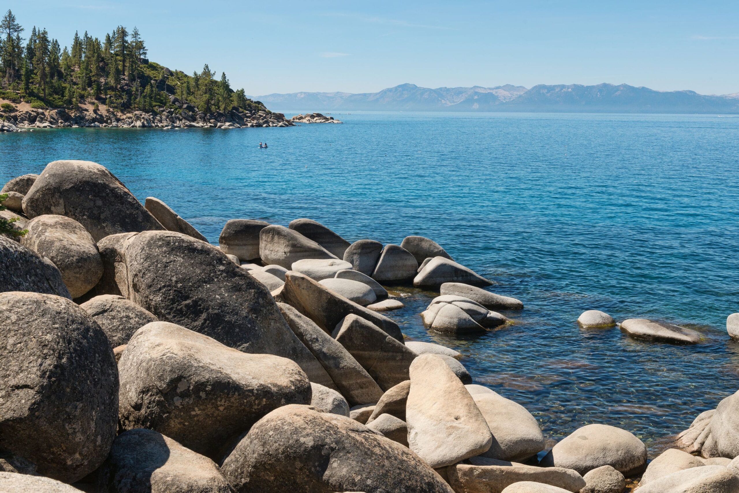 Lake Tahoe with large rocks in the foreground and mountains in the distance