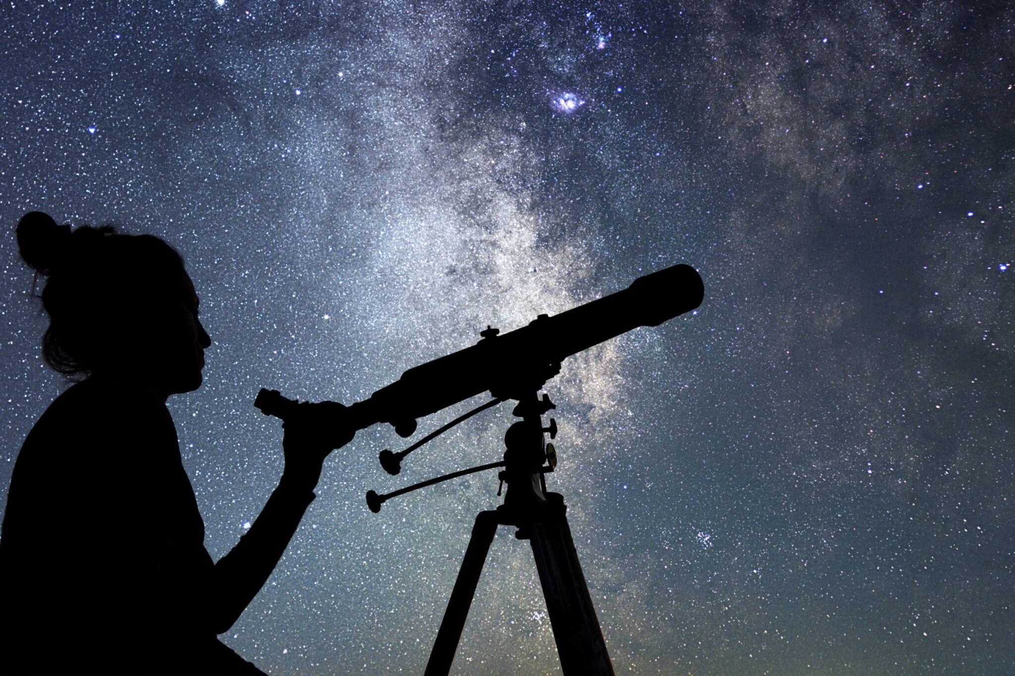 silhouette of a person holding a telescope against a sky full of stars