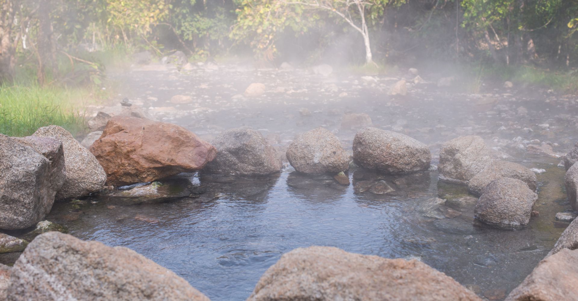 a natural outdoor hot spring emanating steam surrounded b large rocks