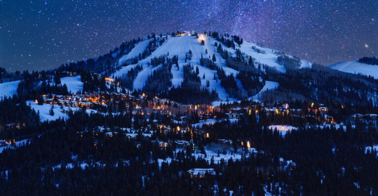 Snow-covered mountain at night, illuminated by bright lights on its peak, creating a serene winter landscape
