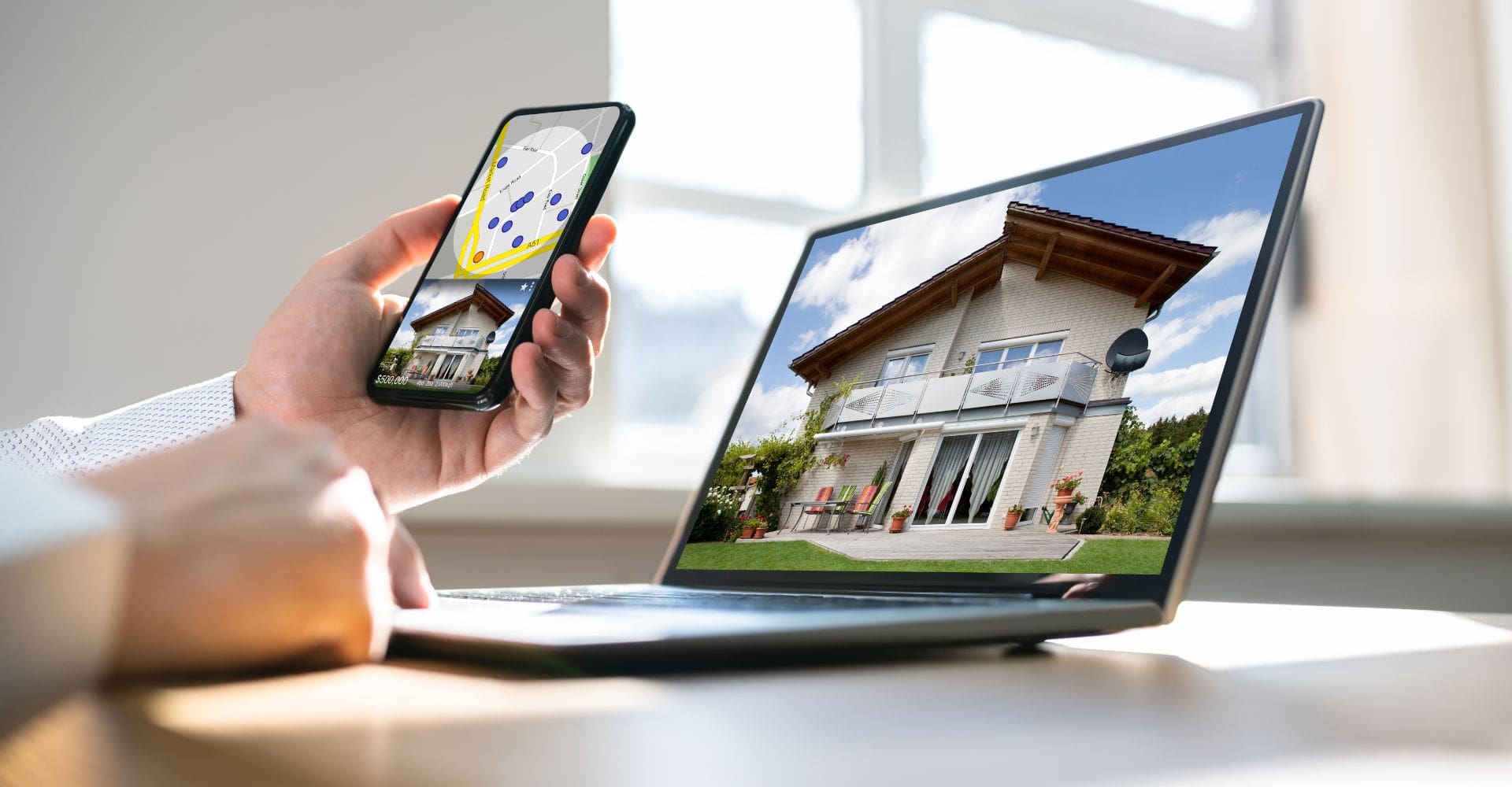 A man views a house on his laptop screen, using a smartphone in his hand for additional information