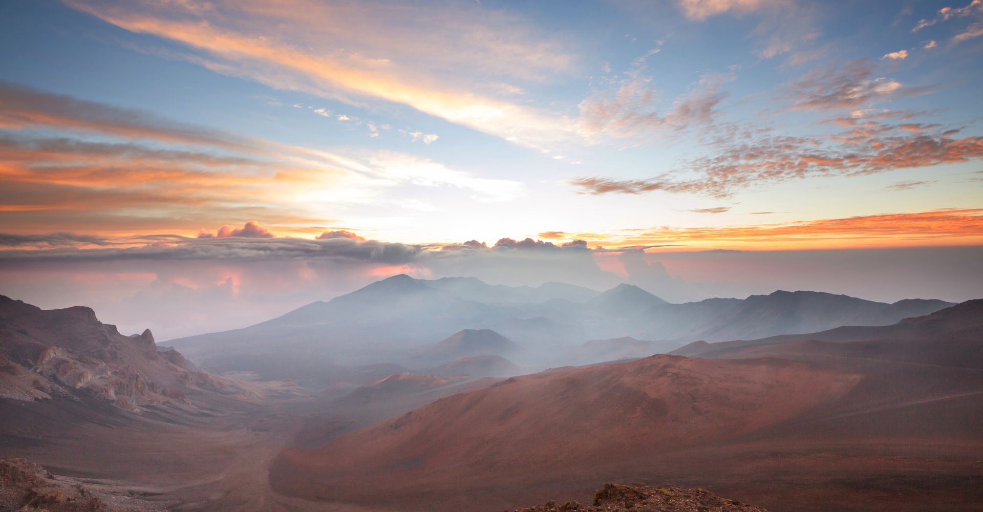 A vibrant sunset casts warm colors over mountains, with fluffy clouds scattered across the sky
