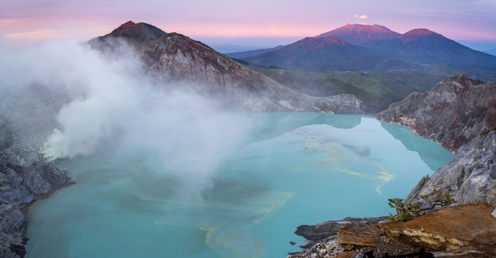 Sunrise casts golden hues over a steaming natural hot springs surrounded by lush greenery