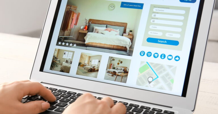 A person browsing a booking website on a laptop, displaying a cozy bedroom image. The screen shows ratings, a map, and booking details.